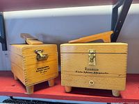 Front view of both wooden shoe shine boxes showing brand names and hardware