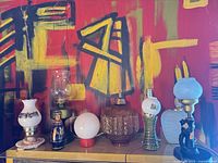 Line-up of eight assorted vintage lamps on shelf against red abstract wall
