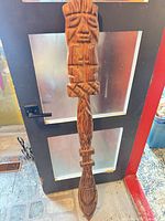 Front view of carved wooden spear wall hanging showing carved face, shaft patterns and pointed end