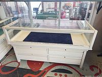 Front view of white wood and glass display case showing glass enclosure, drawers, and dimensions perspective