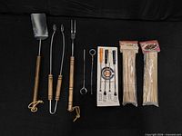 All barbecue and grilling tools laid out: spatula, tongs, fork, loose skewer, packaged skewer set, two bamboo skewer packs