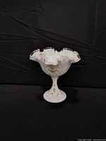 Front view of white ceramic pedestal dish showing ruffled clear-edged rim and floral design