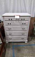 Front view of white dresser showing two small knob drawers and four larger drawers with black pulls