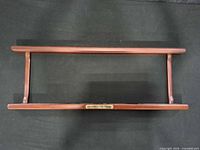 Full view of wooden rectangular display shelf on black background, brass logo plaque visible