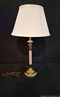 Full view of brass table lamp with pink column, white shade and cord