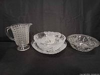 Overall view of the four clear pressed glass pieces: pitcher, serving dish, two bowls