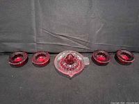 Center citrus juicer and four small matching red tinted glass dishes aligned
