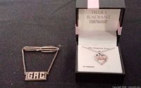 Tie clip with safety chain and monogram plaque alongside boxed heart pendant necklace