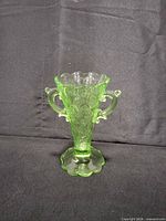 Front view of the green uranium glass vase showing overall form, twin handles and floral embossing
