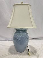 Front view of light blue ceramic table lamp with white square-bell shade and cord