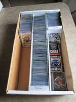Cardboard storage box filled with sleeved football cards, two sealed Ravens playing card decks visible
