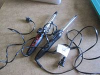 Two curling irons with cords laid on surface