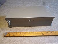 Front view of closed gray metal lock box with ruler for scale