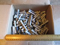 Open box showing large quantity of grey perm rods with ruler for scale