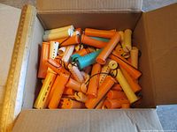 Open box filled with mixed orange, yellow, teal, white perm rods next to ruler