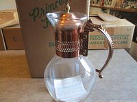 Carafe with copper lid, collar, and handle in front of original Princess House box
