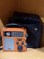 Front view of orange Eton FR-300 radio beside black carry case