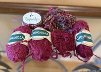 Four magenta Berroco Chinchilla yarn skeins with labels and one multicolour Rapsodya yarn hank