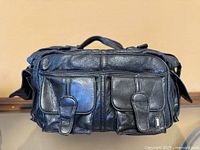 Front view showing leather bag, two front pockets, logo plate