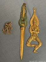Full view of all three brass items: guitar-handle opener, Thai dancer ornament, chain