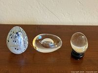 All three glass egg paperweights side by side on tabletop