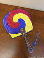 Full view of fan showing three-color swirl pattern, wood handle, blue tassel