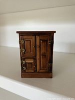 Front view of wood miniature ice box showing paneled doors and metal hardware
