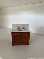 Front view of wooden dollhouse sink cabinet showing doors, countertop, sink cutout and faucets