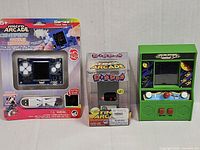 Three mini arcade games: Micro Arcade Centipede / Missile Command blister, Tiny Arcade Dig Dug box, green Galaga tabletop unit