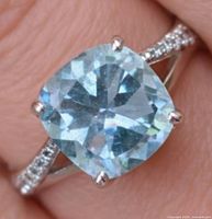 Ring close-up on finger showing blue topaz and CZ shoulders