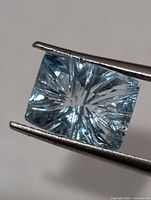Rectangular fantasy-cut blue topaz held by tweezers