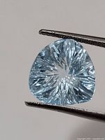 Front view of pale blue fantasy-cut gemstone held by tweezers