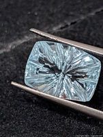Fantasy cut blue topaz held in gem tweezers