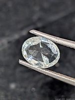 Close-up of oval faceted aquamarine gemstone held by tweezers