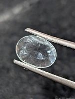 Loose oval aquamarine held by tweezers, showing face-up view