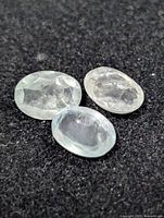 Three oval aquamarine gemstones on dark surface