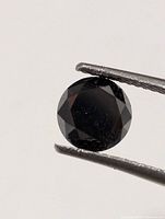 Round faceted black diamond held by tweezers, showing overall shape and color