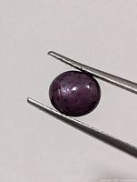 round cabochon star ruby held by tweezers front view