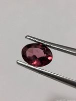 Oval faceted garnet held in tweezers, front view shows color and clarity