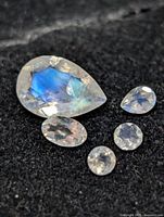 Five faceted moonstone gemstones on black background, showing cuts and blue sheen