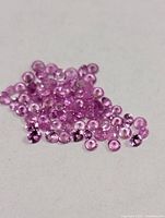 Pile of small round faceted pink sapphires on light background