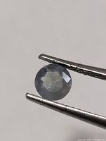 Round Alexandrite held in tweezers, showing faceted cut and overall color