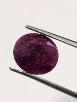 Front view of oval faceted ruby held by tweezers