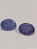 Two oval blue-violet faceted stones on neutral background