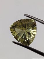 Triangular lemon quartz held by tweezers, frontal view showing starburst facets