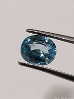 Front view of oval blue zircon held by tweezers