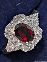 Front view of silver ring with oval red garnet and surrounding cubic zirconia halo