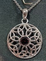 Front view of silver pendant necklace showing interlaced design and garnet center