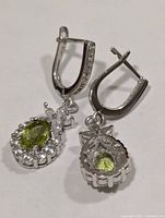 Front and rear views of both earrings showing peridot centers, CZ halos, lever backs, and silver setting