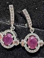 Close-up of both earrings showing ruby centres, CZ halo, and stone-set bails